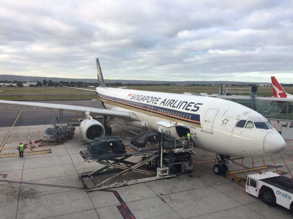 A Singapore airlines aircraft docked at the airport, with men loading cargo into the hold