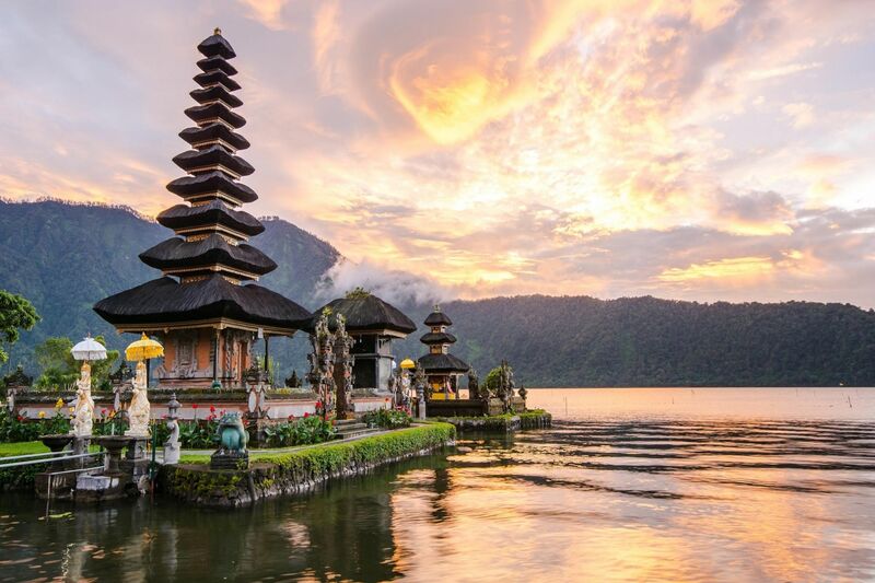 Balinese temple on the banks of a lake with mountains in the background at sunset