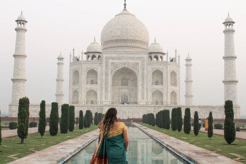 Woman in red, green and gold Indian Saree facing the Taj Mahal