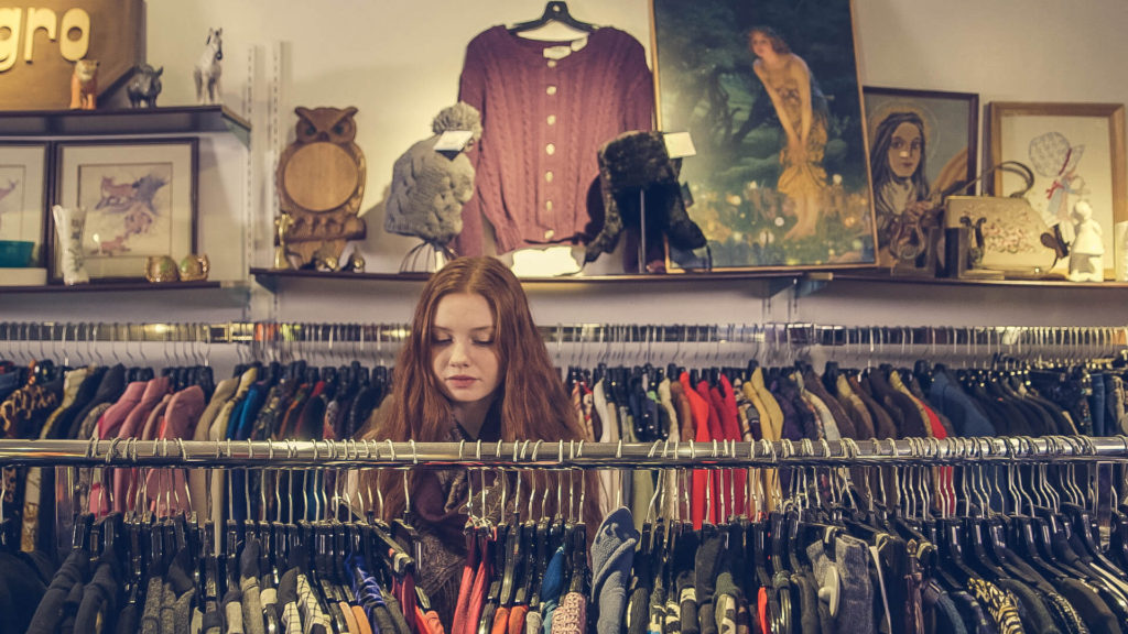 a young girl is looking through racks of clothing