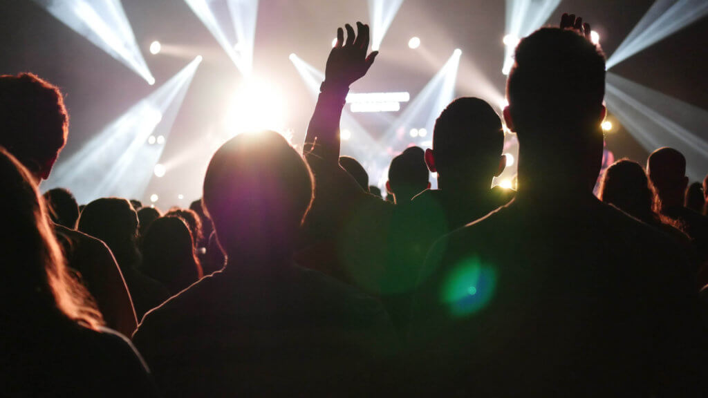 a crowd of people, in silhouette, are dancing at a party with strobe light flashing in the distance