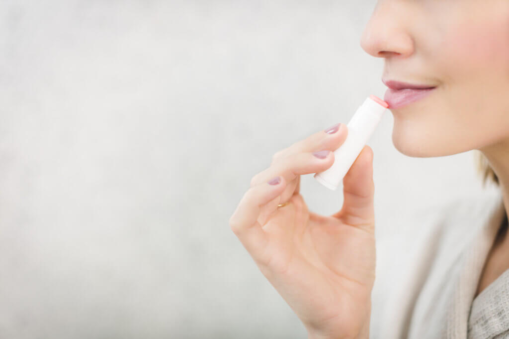 a ladies nose, lips and chin in frame. the lady is applying lip balm to her lower lip