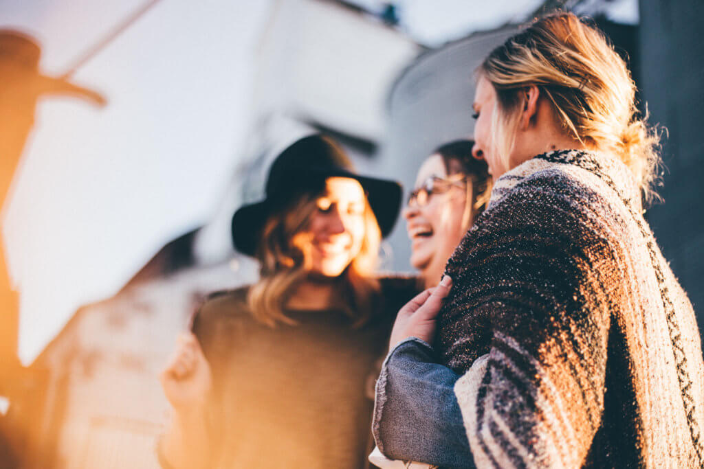 three women are networking at a travel conference. the sun is shining on their faces, the two outer women are looking inward toward the middle woman