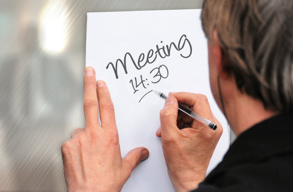 a man has written the words meeting 14:30 on a piece of paper in black pen. he is underlining the time