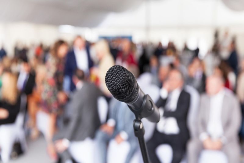 a microphone front and centre with an audience of people in the background, blurred with no detail