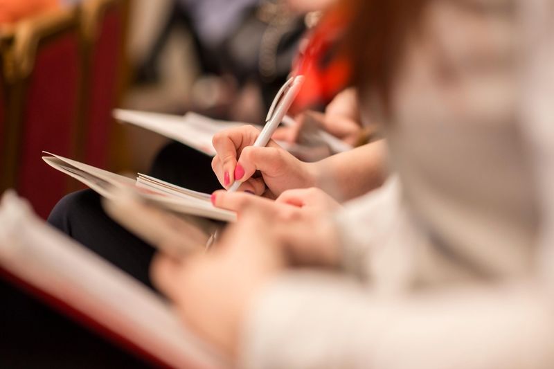 blurred people sitting in a row of chairs scribbling notes in their notebooks