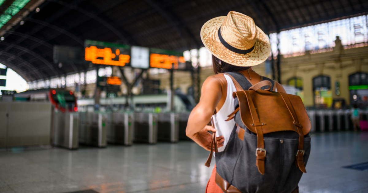 what to pack in your carry-on showing a lady wearing a backpack. she is faced away from the camera and looking toward trains at a train station