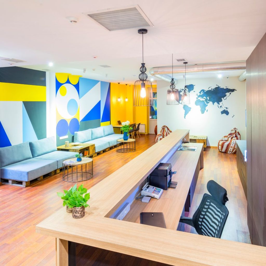 a brightly decorated hostel lobby with the check-in desk in view, a map of the world painted on the far wall and some seating for guests 