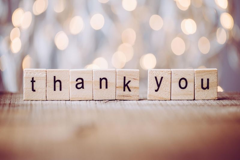 the word thank you spelt out in wooden blocks in front of blurry fairy lights