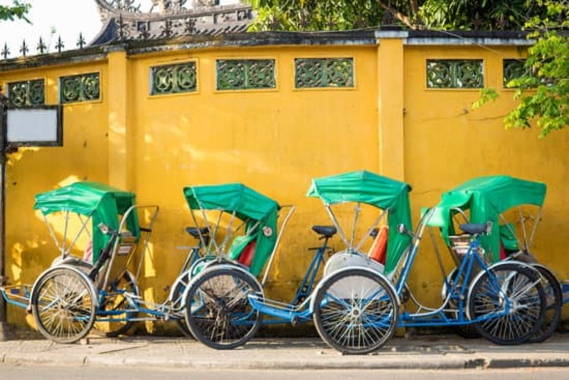 Cyclo tuk tuks lined up against a bright yellow wall in HoiAn, Vietnam