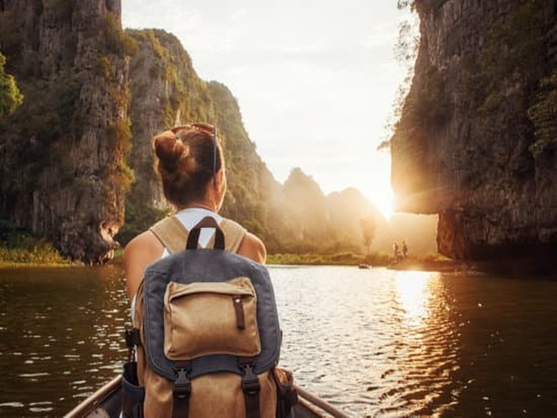 Woman travelling by boat through the karst mountains of Tam Coc, Vietnam, Southeast Asia. She is facing forward with back pack on enjoying the sunset.