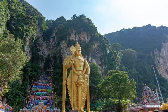 250 rainbow colour stairs leading to Batu Caves in Malaysia. a huge gold statue stands guard at the base of the stairs. the outside of the caves re covered in lush green rainforest