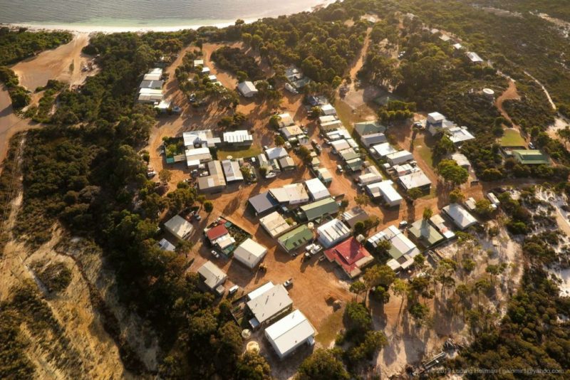 an aerial top down drone image of the Duke of Orleans Bay Caravan Park in Esperance. the campground is in the dusty red sand dunes, surrounded by bushland and with the beach at the top of the image