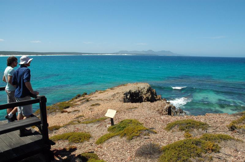 two men stand at Point Ann viewing platform looking over a cliff into the vast ocean expanse that is Bremer Bay. there are some hills off into the distance as the shoreline disappears