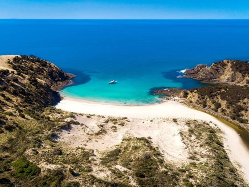 An aerial view looking down toward Western River cove. There is a rocky headland to the left and right of the image with the beautiful white sandy beach in the centre of the image. Western River can be seen reaching the ocean from the right of the image