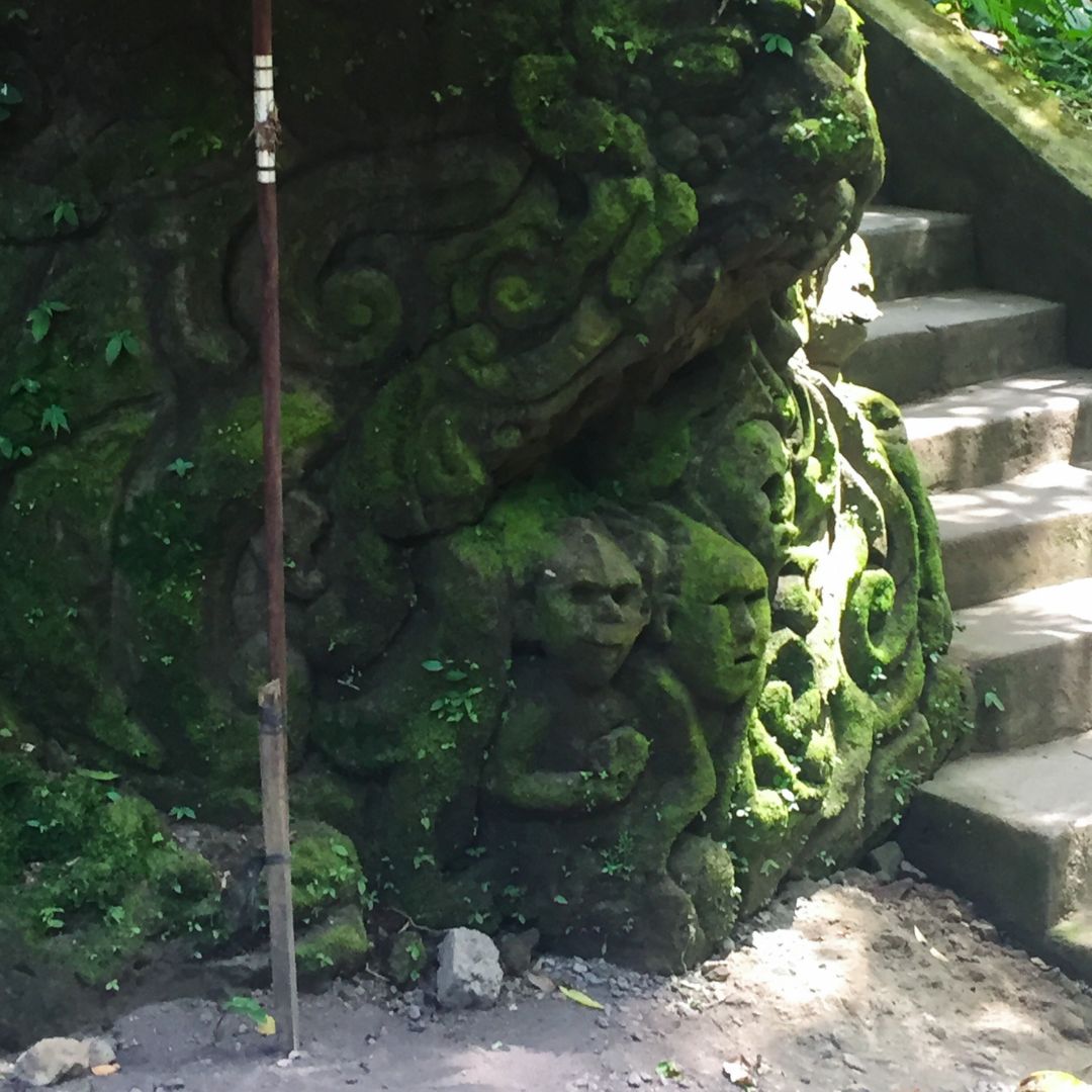 carved monkeys and faces into the rock wall, next to the stairs down to the waterfall. the rocks are covered in green moss