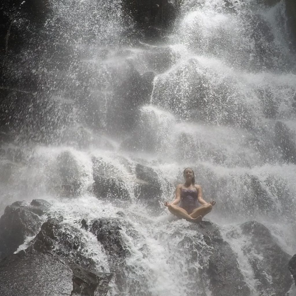 Luisa sitting under the waterfall at Kanto Lampo. she is sitting with crossed legs and her arms resting on her knees