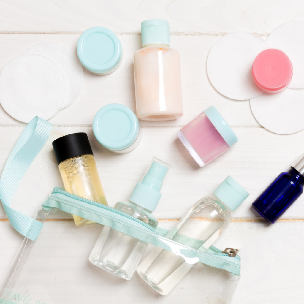 lots of min travel sized beauty bottles and containers spilling out of a clear toiletry bag. each lid is an light blue colour and the zip on the bag is the same colour. there is one bottle with a black lid and a dark blue bottle with a silver lid