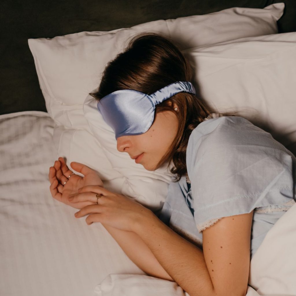 a woman is lying in bed with a purple eye mask on her eyes which is necessary for a hostel