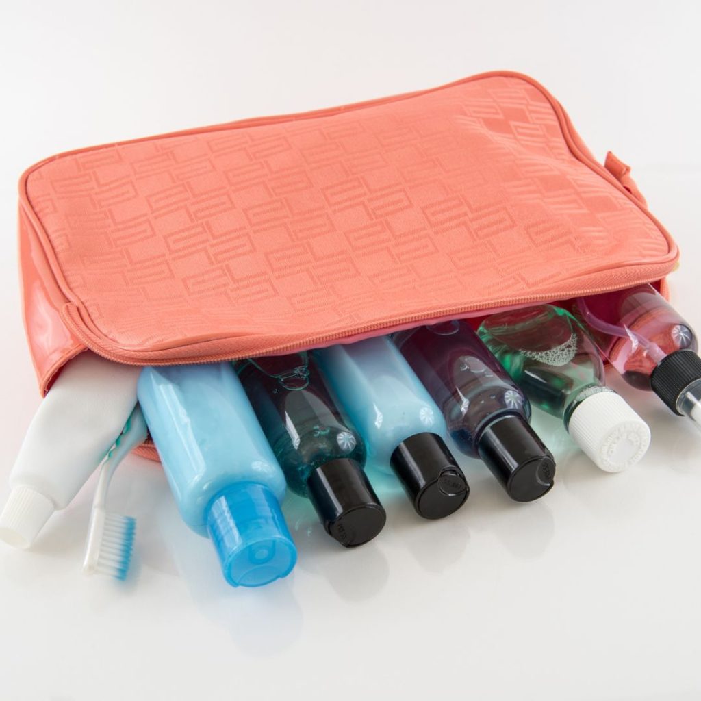 a pink toiletry bag with many travel sized toiletries perfect for the hostel dorm room. The bottles are resting half in the bag and half out. 