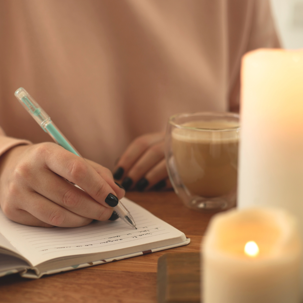 a woman with black fingernails is writing in her journal with a cup of coffee and lit candles on the table