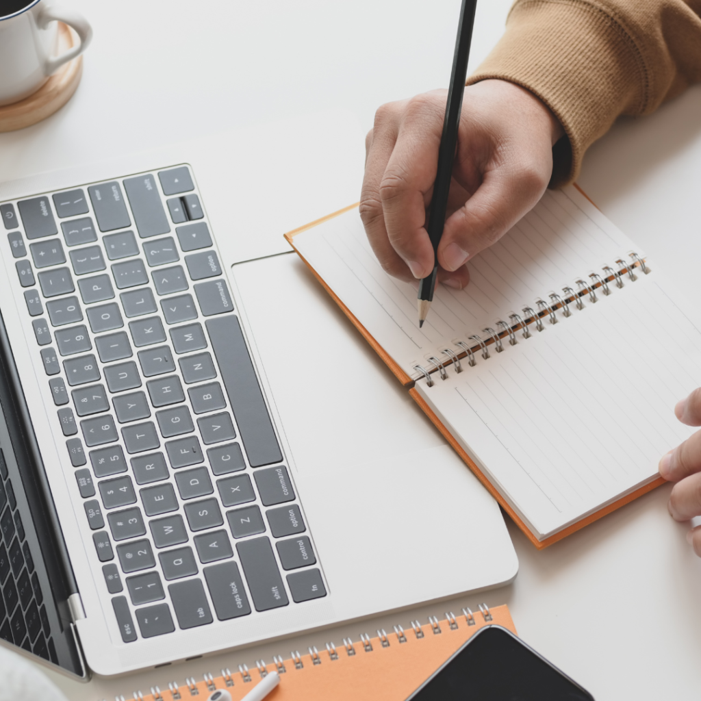 a laptop is on screen on the left and a person with only their hand visible is writing in a notebook while watching an affiliate marketing course for beginners